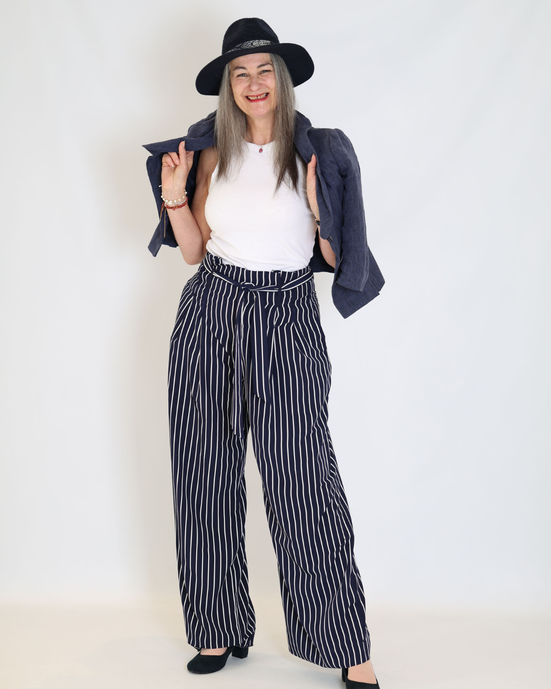 Jacqueline Carson smiling in a black hat, white top, and navy striped trousers